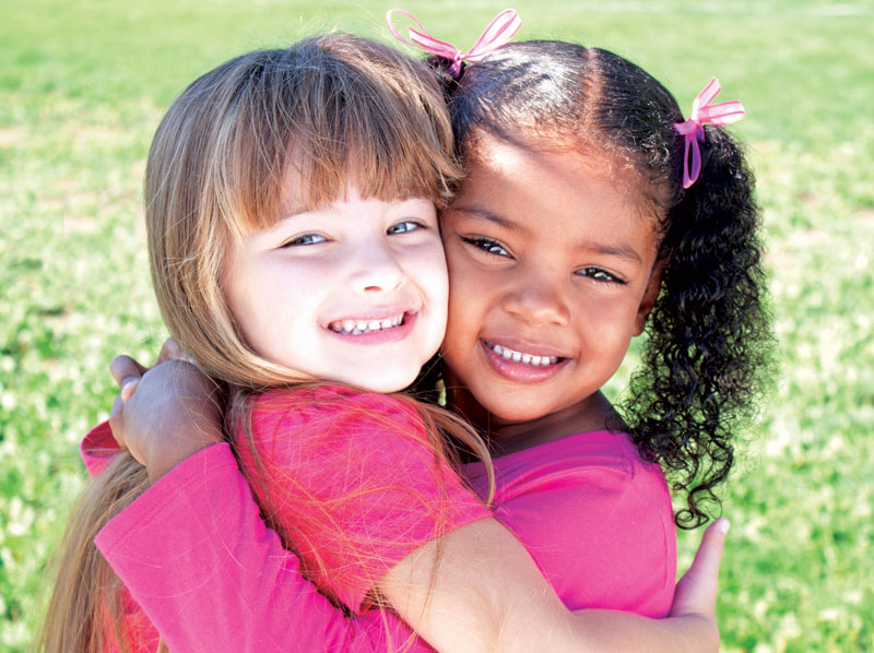 Two young girl friends hugging and smiling.